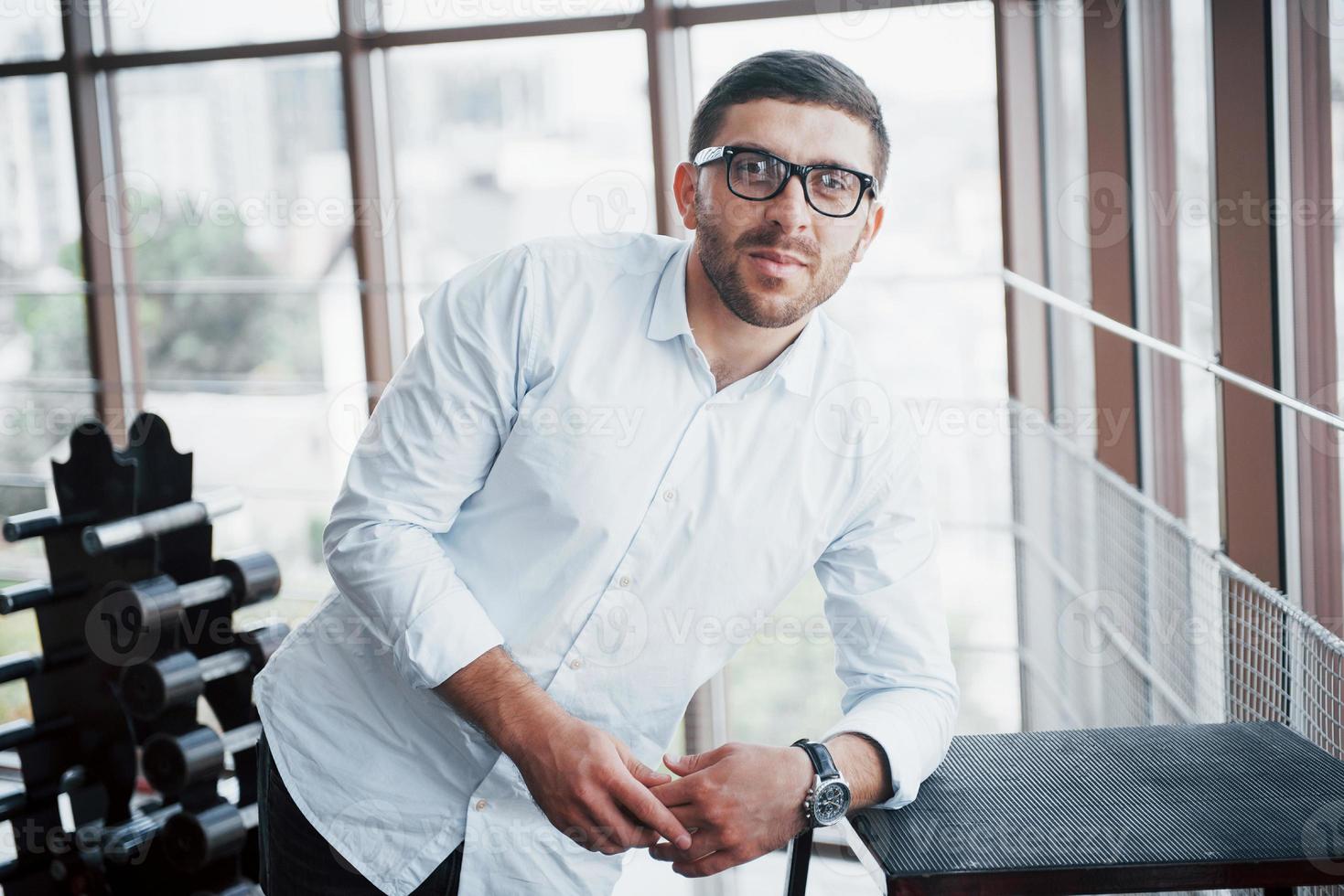 un bel ragazzo seduto sul pavimento in palestra, in camicia bianca e pantaloni. concetto di sport foto