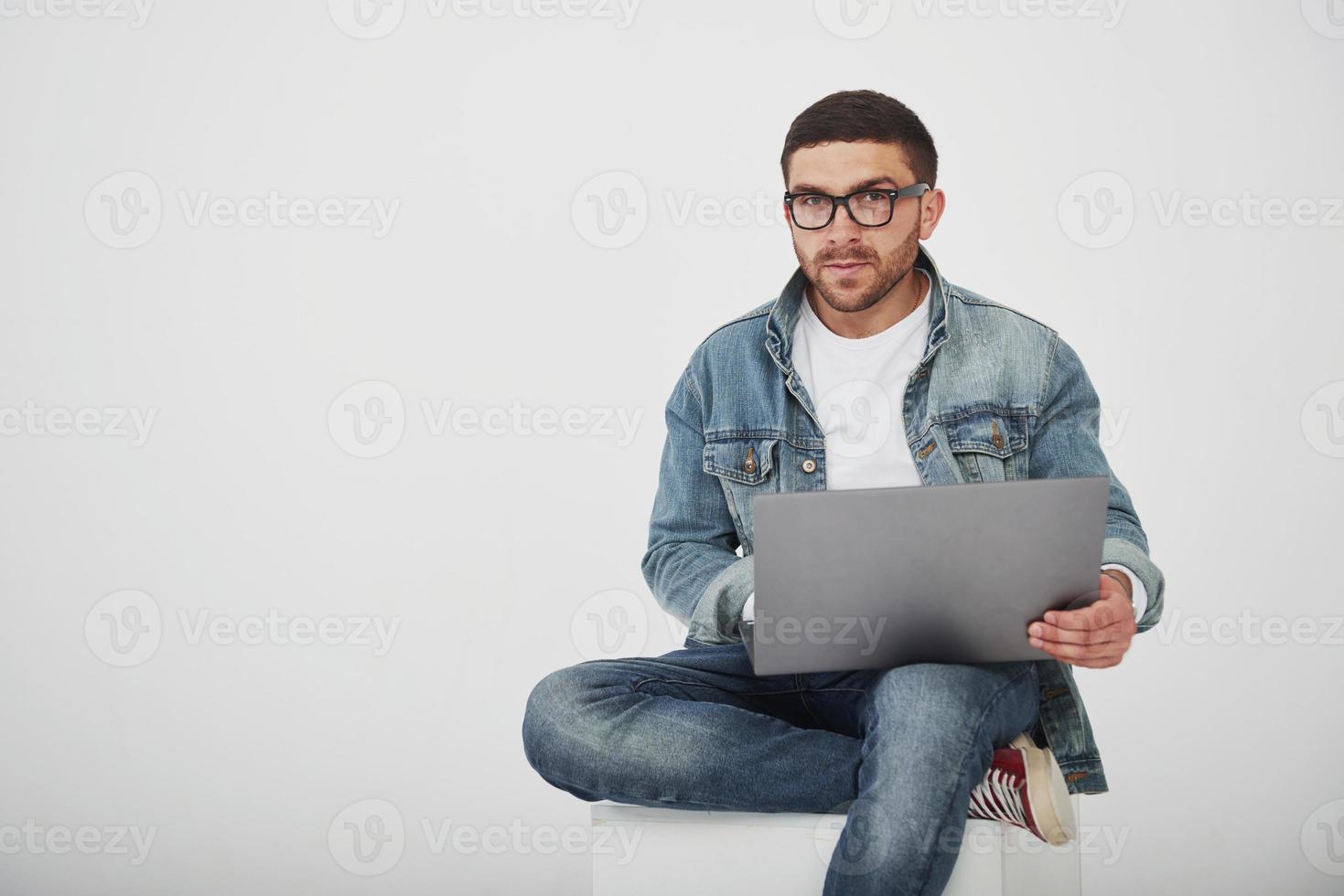 bel giovane con laptop e controlla il suo orario su sfondo bianco foto