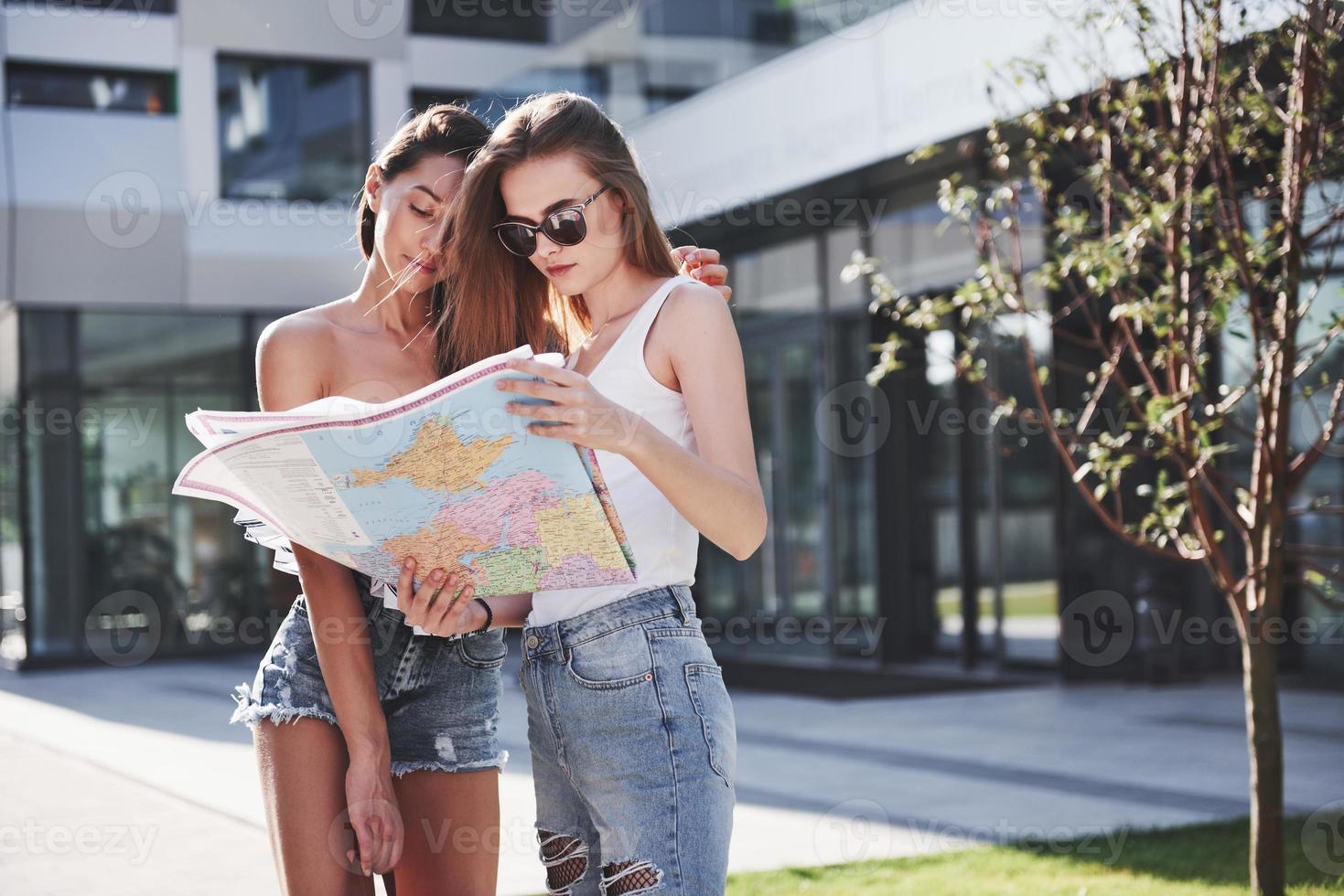 ragazze che leggono la mappa della città e cercano un hotel. adorabili turisti con zaini determinano il concetto di conoscenza del mondo foto