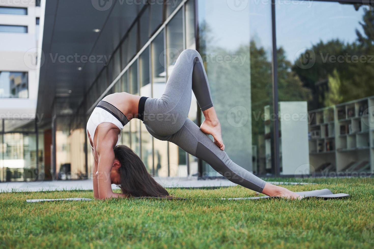 mattina di sole estivo. giovane donna atletica che fa verticale sulla strada del parco cittadino tra moderni edifici urbani. esercizio all'aperto stile di vita sano foto