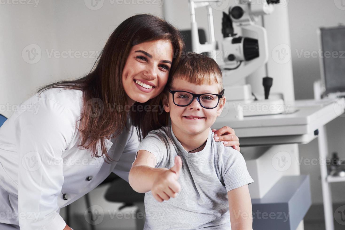 giovane medico biondo femminile attraente che sorride con il suo piccolo paziente soddisfatto. gli occhiali sono perfettamente selezionati foto