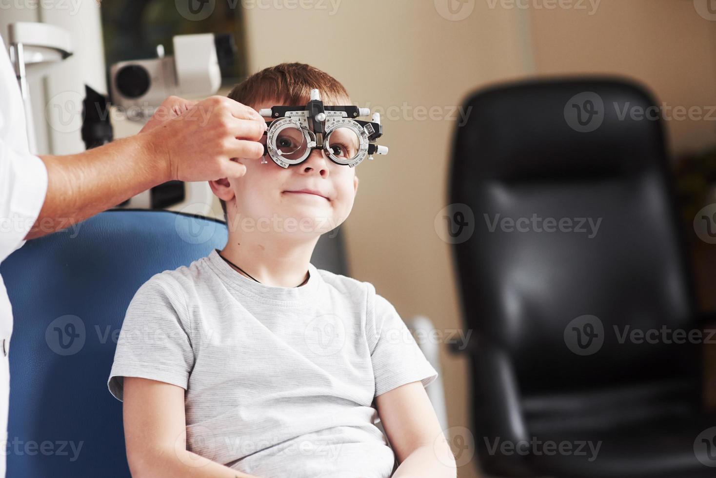 controllando lenti diverse. bambino seduto nell'armadietto del medico e ha testato la sua acuità visiva foto