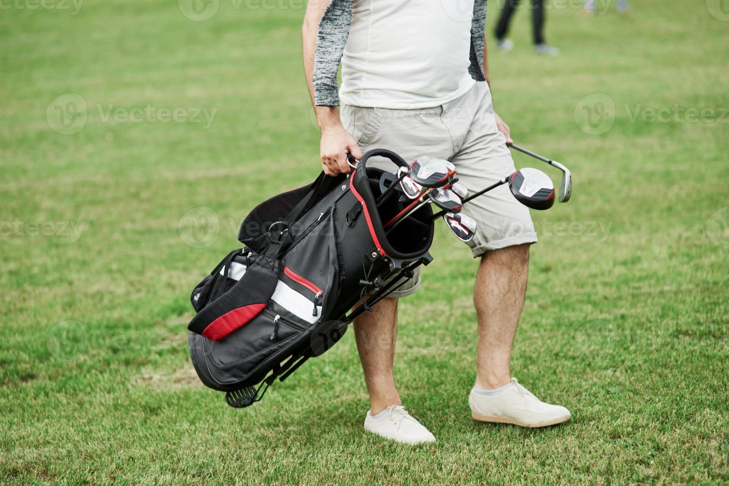 foto ritagliata di un uomo che tiene in mano una borsa con bastoncini da golf mentre cammina sul prato verde