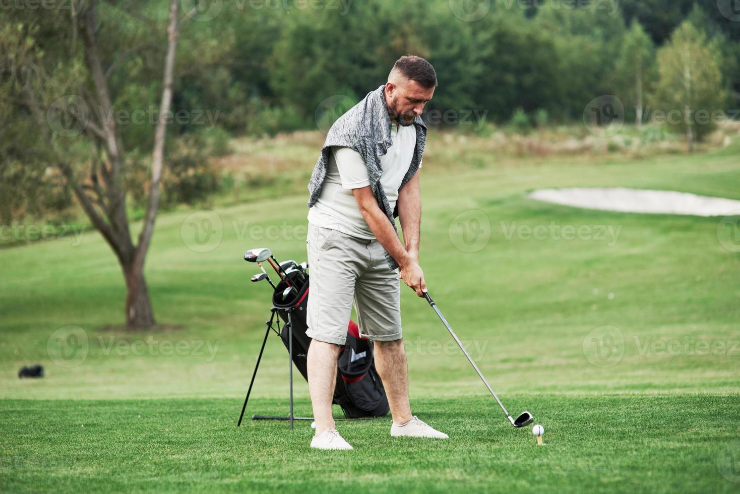 uomo barbuto adulto che si concentra a giocare a golf nello splendido prato verde foto