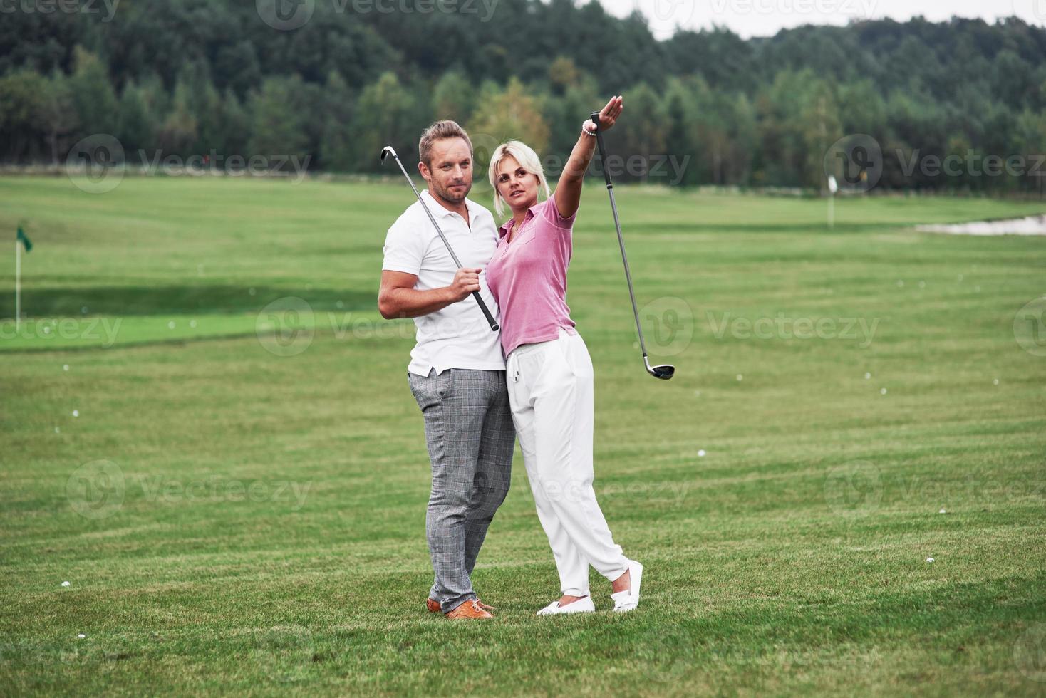 la donna vuole andare dall'altra parte. coppia di giocatori di golf con bastoni in mano in piedi sul prato foto