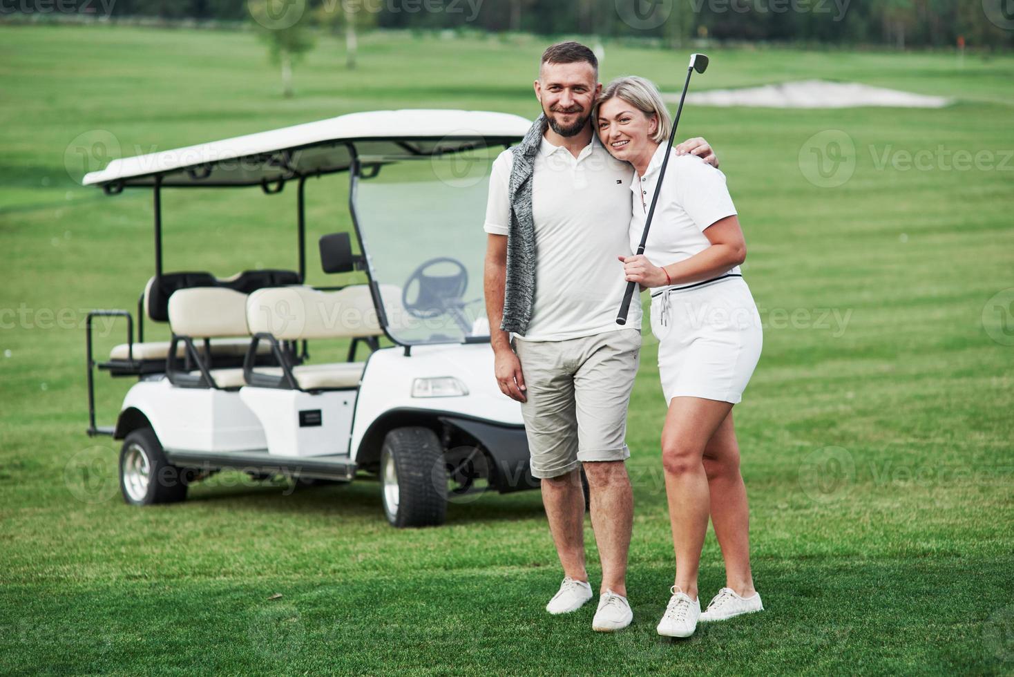 coppia di due giocatori di golf che stanno sul prato verde con un carrello dietro di loro foto