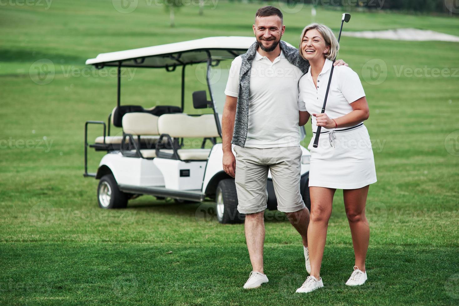 sentirsi felice. coppia di due giocatori di golf che stanno sul prato verde con un carrello dietro di loro foto