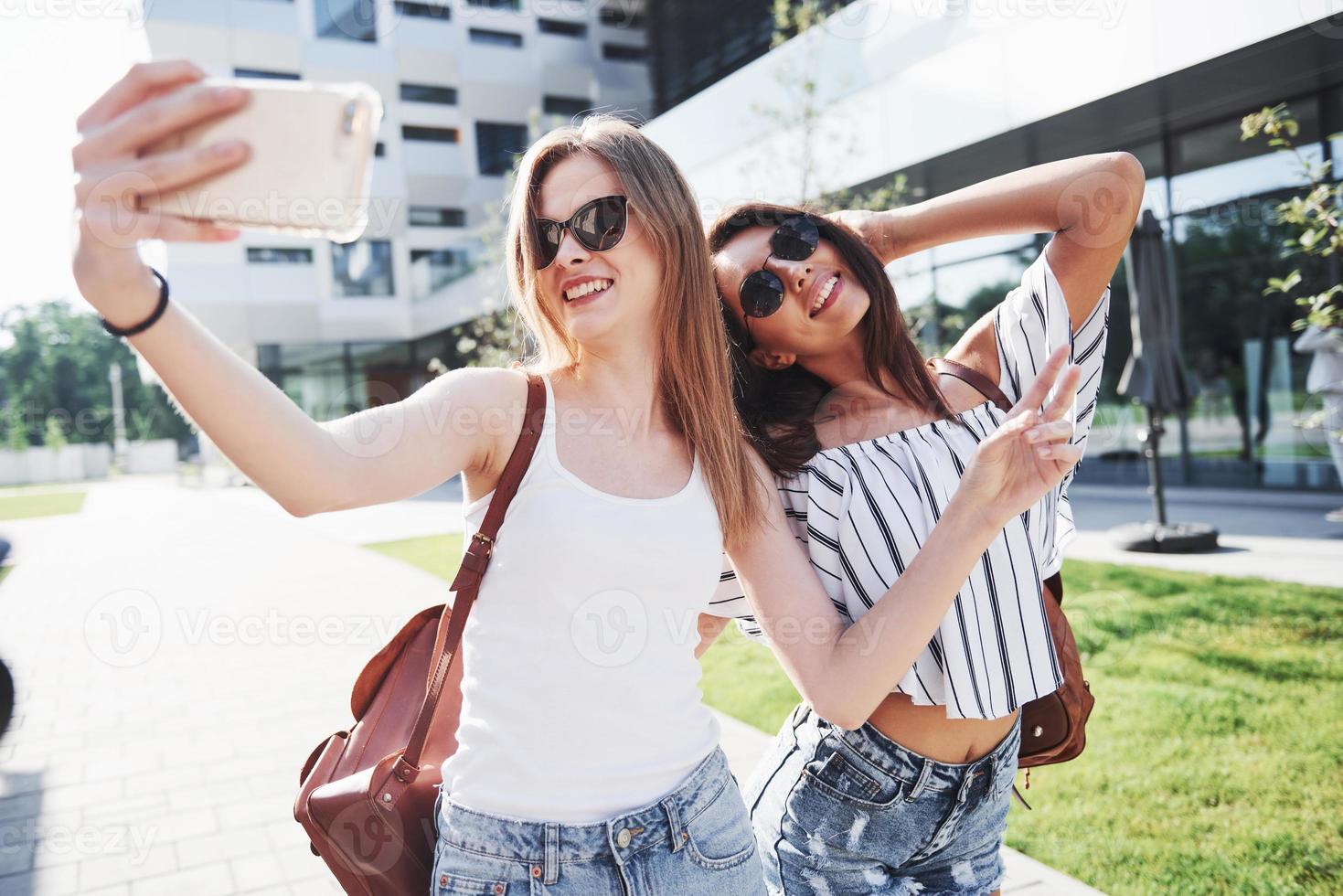 due belle ragazze con zaini camminano insieme in città. amici carini condividono i segreti foto