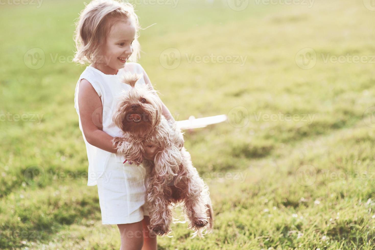 sorridente ragazza allegra che tiene in braccio un cagnolino e gioca con lui fuori nel campo foto