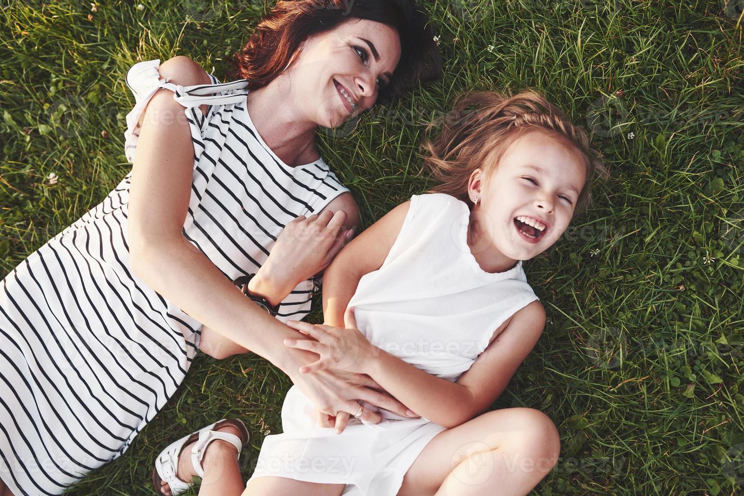 giocando e sorridendo. vista dall'alto di bambini e madre sdraiati sull'erba piena di sole e guardandosi l'un l'altro foto