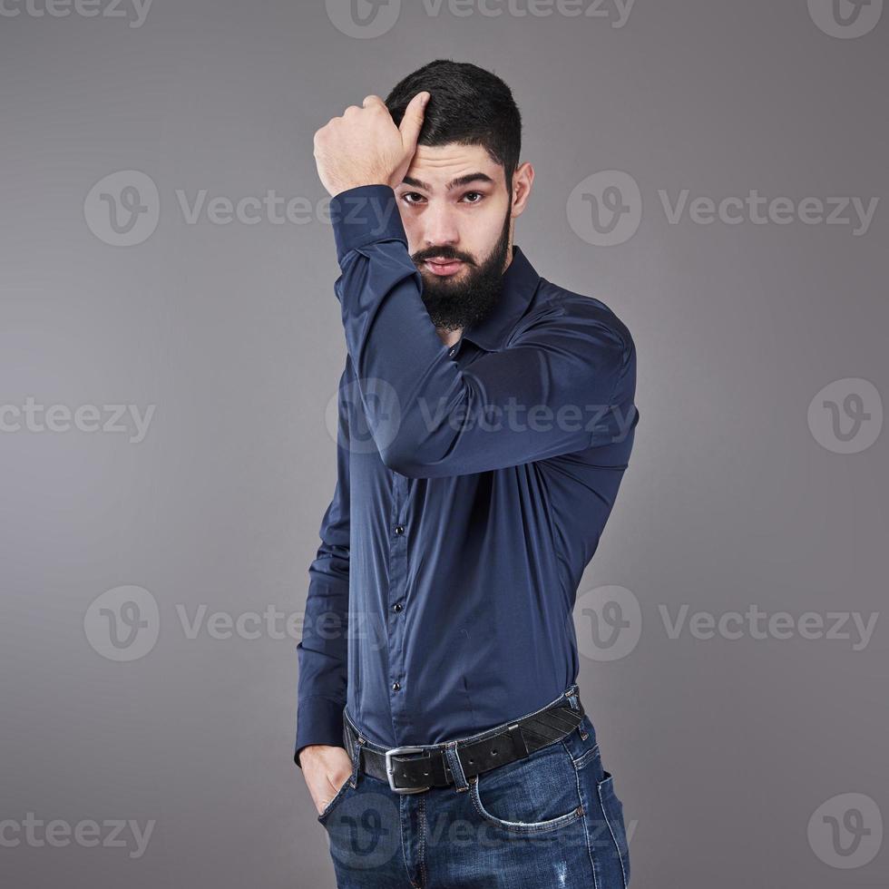 bel giovane uomo barbuto sta guardando lontano mentre in piedi su sfondo grigio foto