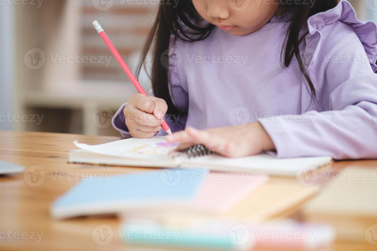 un' giovane ragazza è scrittura con un' rosso matita su un' pezzo di carta foto