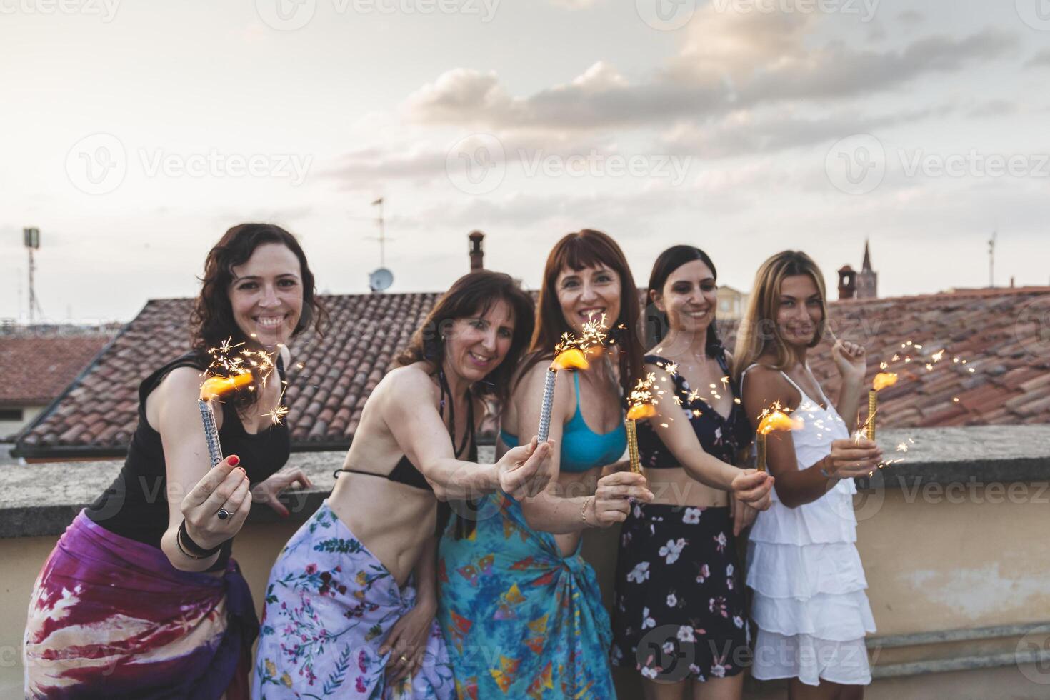 gruppo di contento femmina amici Tenere sparklers a tetto festa foto