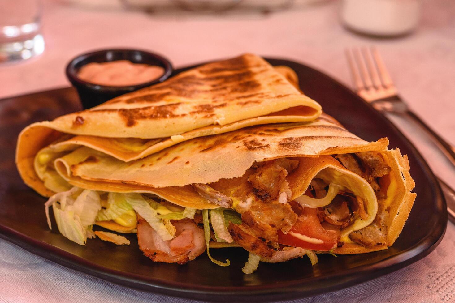 grande pancake pieno con pollo con formaggio, Bacon, pomodoro, lattuga, salsa su un' nero piatto nel greco taverna. magro Pancakes, crepes. mediterraneo cucina. selettivo morbido messa a fuoco foto