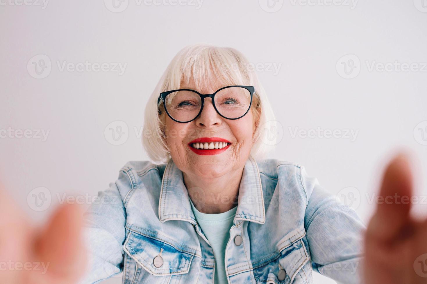 donna anziana alla moda con i capelli grigi e in giacca di jeans e occhiali che ti abbraccia o fa selfie. amore, abbracci, anti età, concetto di vibrazioni positive foto