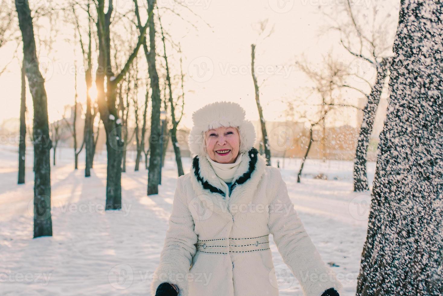 donna anziana in cappello bianco e pelliccia che tiene la neve nelle mani nella foresta di neve. inverno, età, concetto di stagione foto