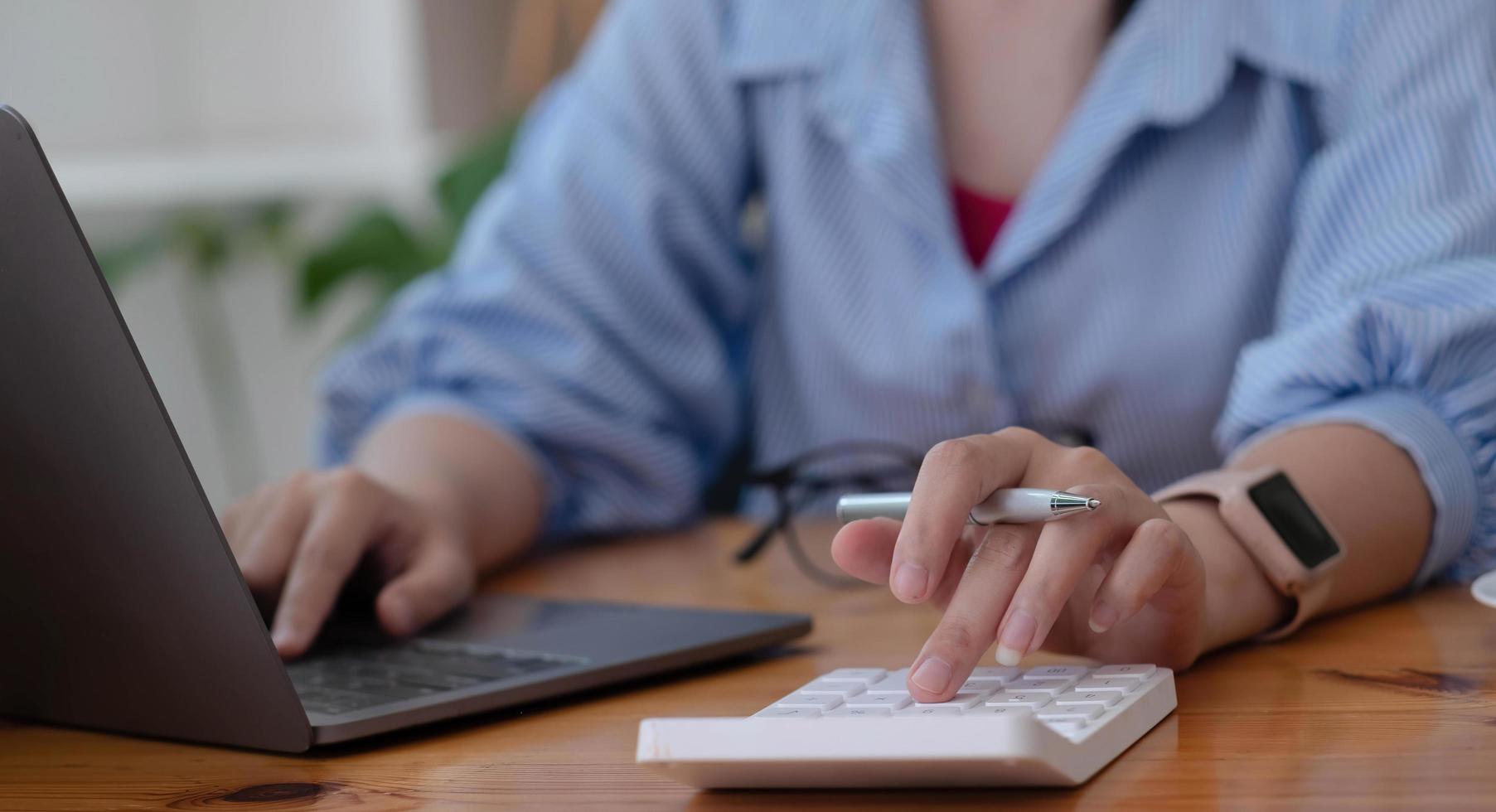 primo piano donna d'affari che utilizza calcolatrice e laptop per fare finanza matematica sulla scrivania di legno in ufficio e sfondo di lavoro aziendale, tasse, contabilità, statistiche e concetto di ricerca analitica foto