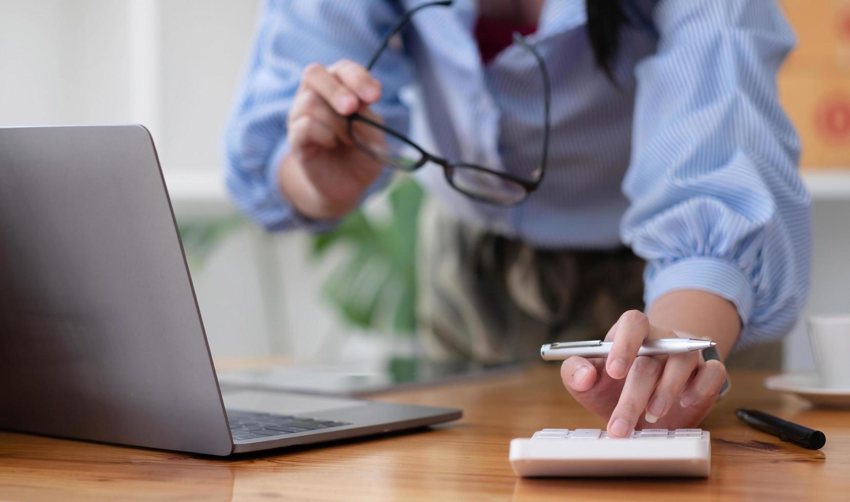 primo piano donna d'affari che utilizza calcolatrice e laptop per fare finanza matematica sulla scrivania di legno in ufficio e sfondo di lavoro aziendale, tasse, contabilità, statistiche e concetto di ricerca analitica foto