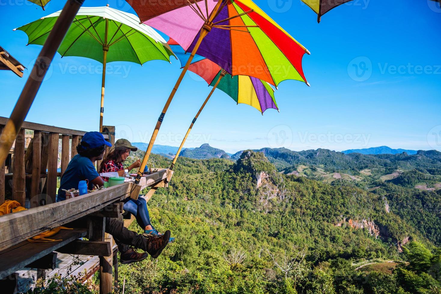 turisti asiatici coppia seduta mangiare noodle sulla piattaforma di legno e guardando la vista panoramica delle montagne della natura bellissima a ban jabo, mae hong son, thialand. foto