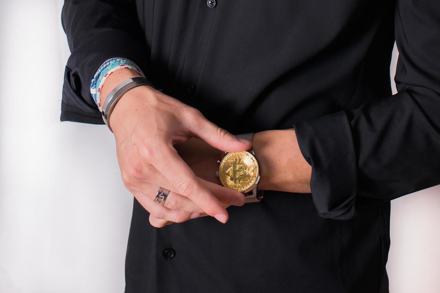 mani di un giovane con un bitcoin sull'orologio. camicia nera, bracciali moderni. foto