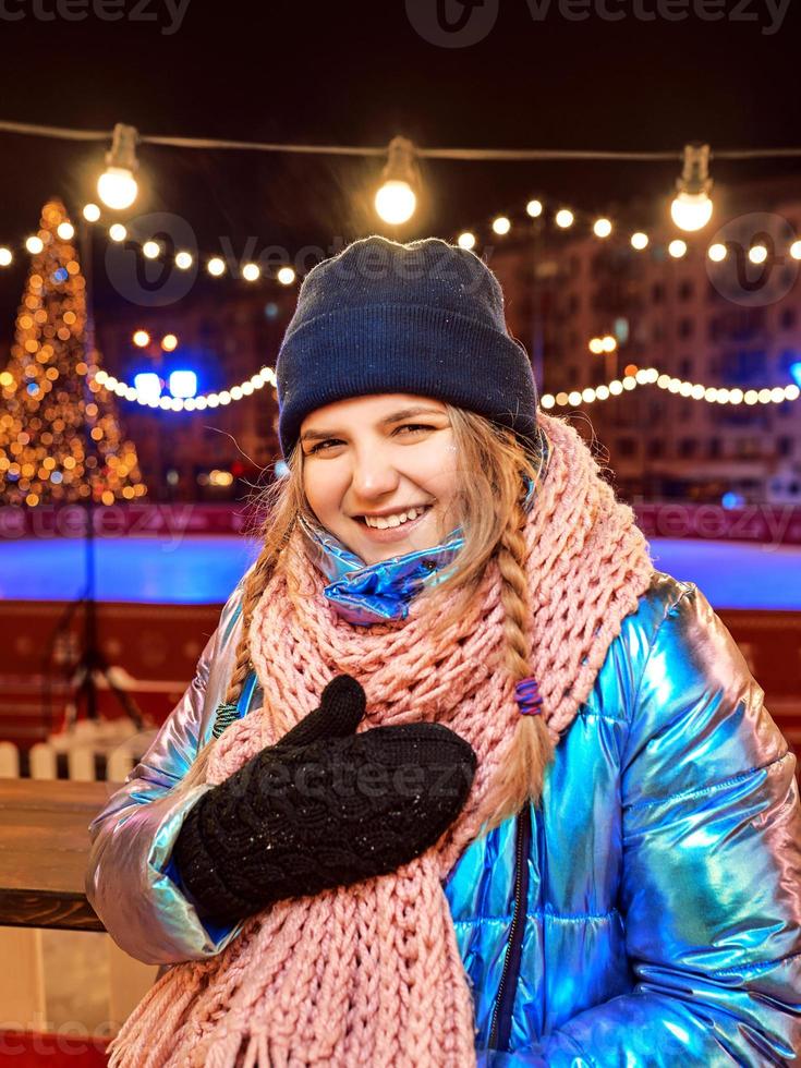 felice sorridente giovane donna caucasica in sciarpa, cappello, giacca, guanti sulla pista di pattinaggio all'aperto. anno nuovo, divertimento, concetto invernale foto