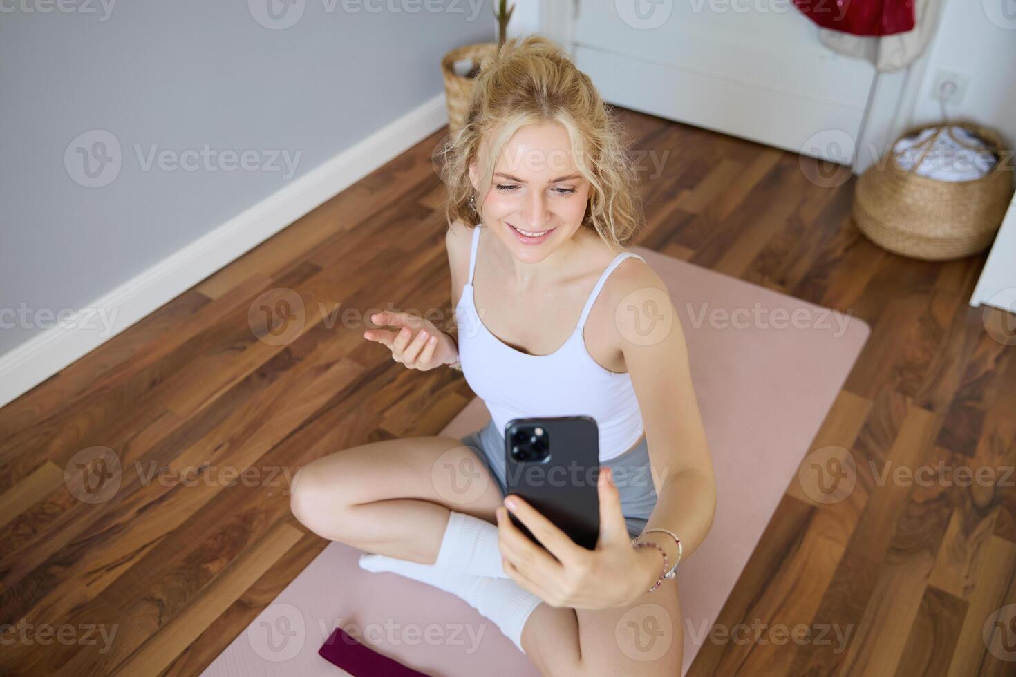 giovane sportivo fitness allenatore, yoga istruttore fa vivere flusso, prende selfie su smartphone mentre seduta su gomma da cancellare stuoia a casa, registrazione sua allenarsi formazione sessione foto