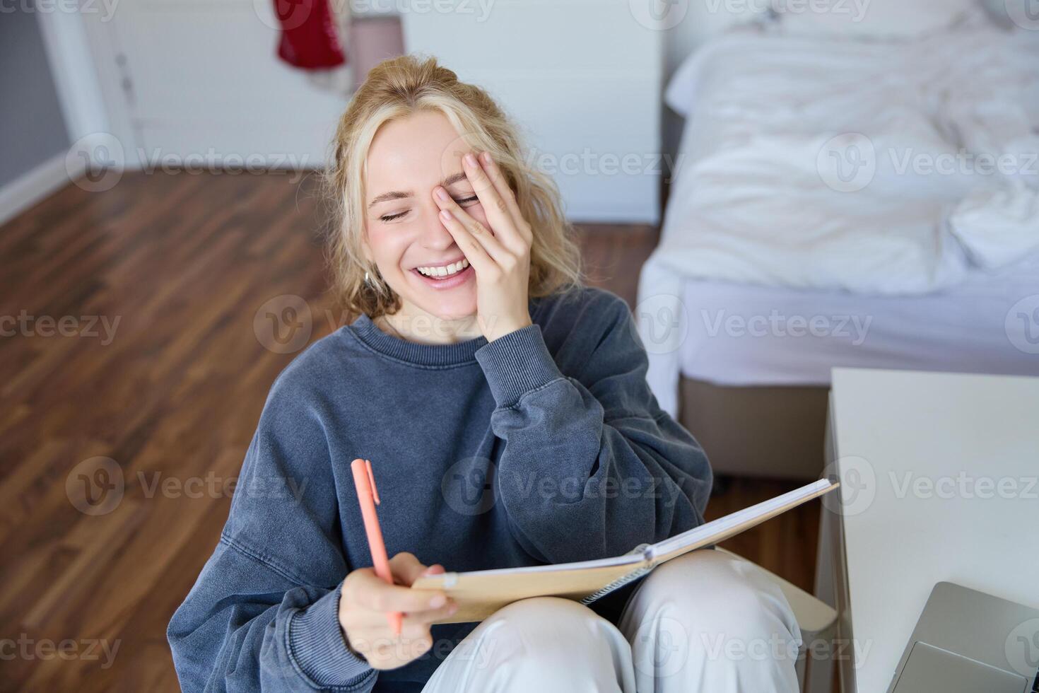 ritratto di carismatico biondo ragazza, sorridente donna nel Camera da letto, Tenere taccuino e penna, scrittura nel rivista o diario, crea per fare elenco nel progettista foto