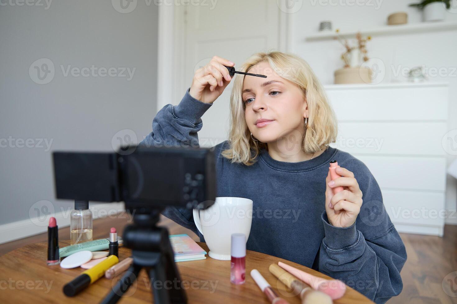 ritratto di biondo sorridente donna record un' stile di vita blog, vlogger o trucco artista registrazione per sociale media, Tenere mascara, rivedere bellezza prodotti per seguaci in linea foto