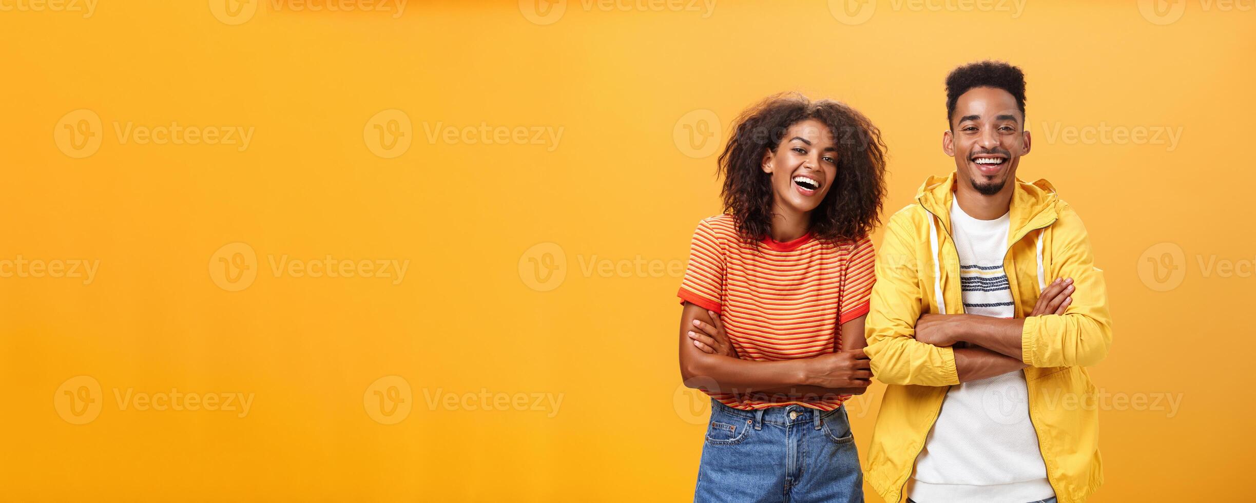 Due africano americano uomo e donna essere migliore amici ridendo su forte Guardando divertente film nel cinema tutti vestito su nel elegante attrezzatura in piedi con mani attraversato su il petto e divertito espressione foto