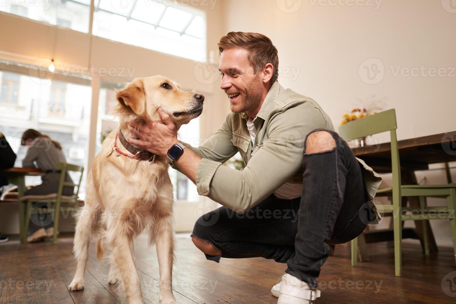 ritratto di contento giovane uomo entra caffè negozio con il suo d'oro recuperatore. bello tipo petting cane nel cucciolo amichevole bar foto