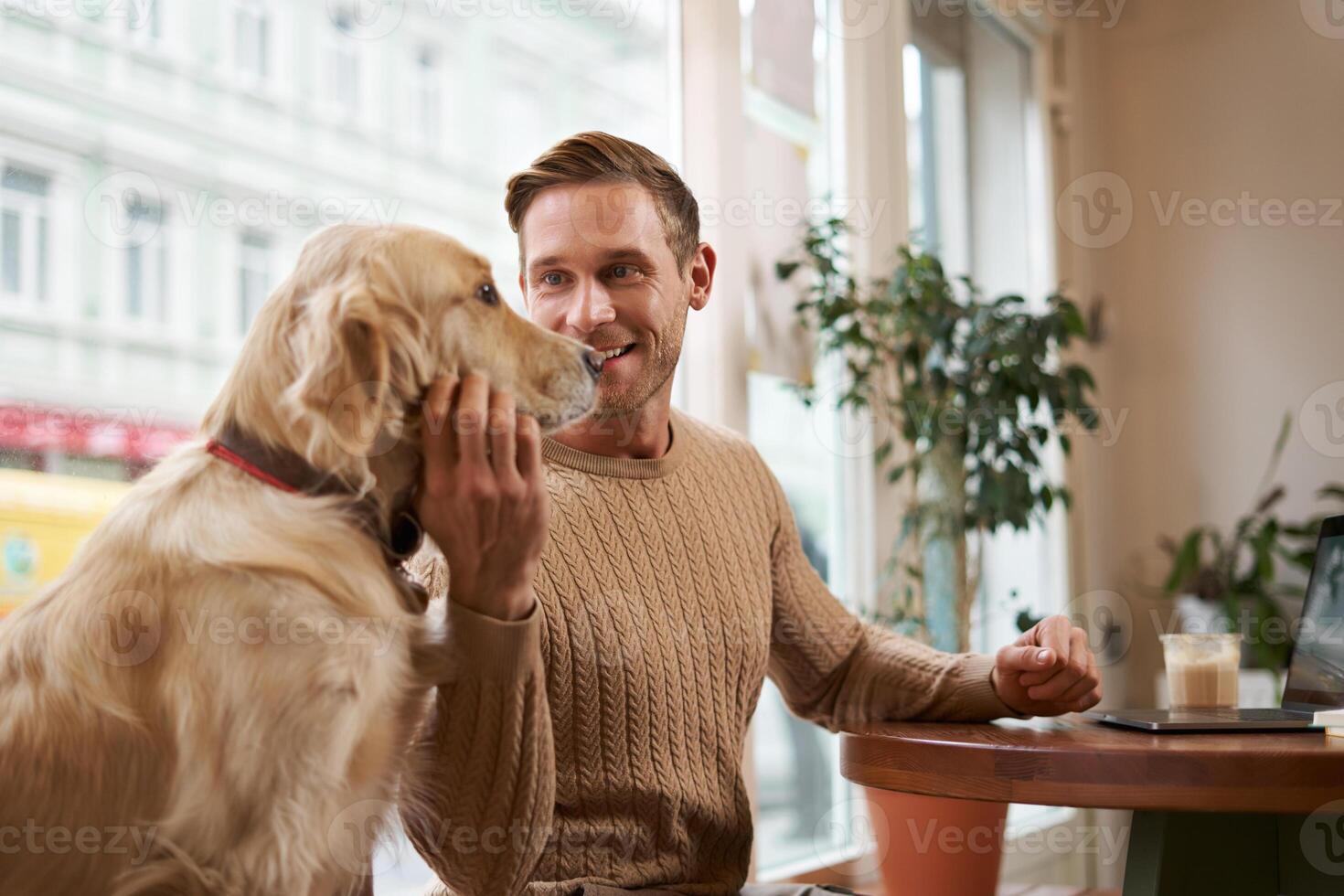 stile di vita foto di giovane bello uomo, imprenditore Lavorando nel un' bar su il computer portatile mentre il suo cane si siede Il prossimo per lui. un' tipo animali domestici il suo d'oro cane da riporto mentre utilizzando computer nel un' caffè negozio