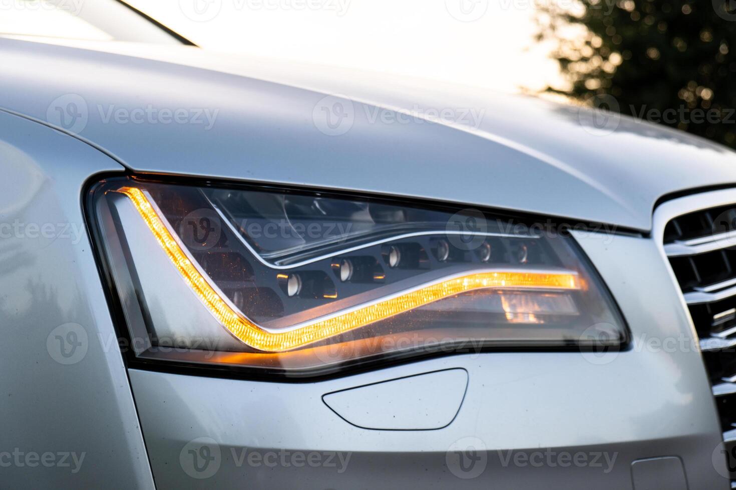 faro trasformato su nel pulito auto dopo lavaggio lusso argento macchina. berlina auto esterno di moderno lusso auto durante tramonto su autostrada strada. dettagli di davanti proiettore. prestigio sport automobile foto