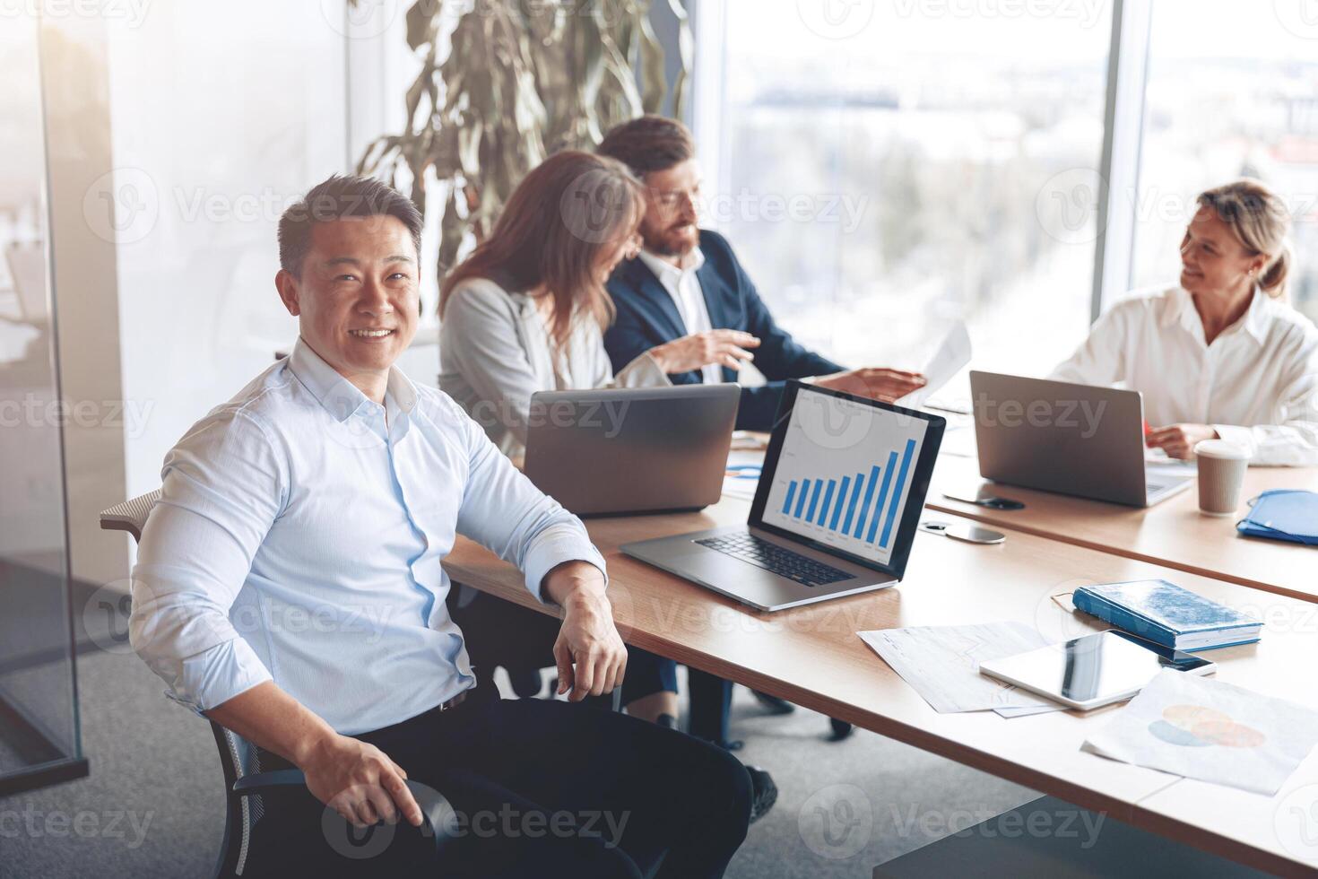 ritratto di sorridente asiatico uomo d'affari Lavorando su un' il computer portatile durante un' incontro con un' squadra foto