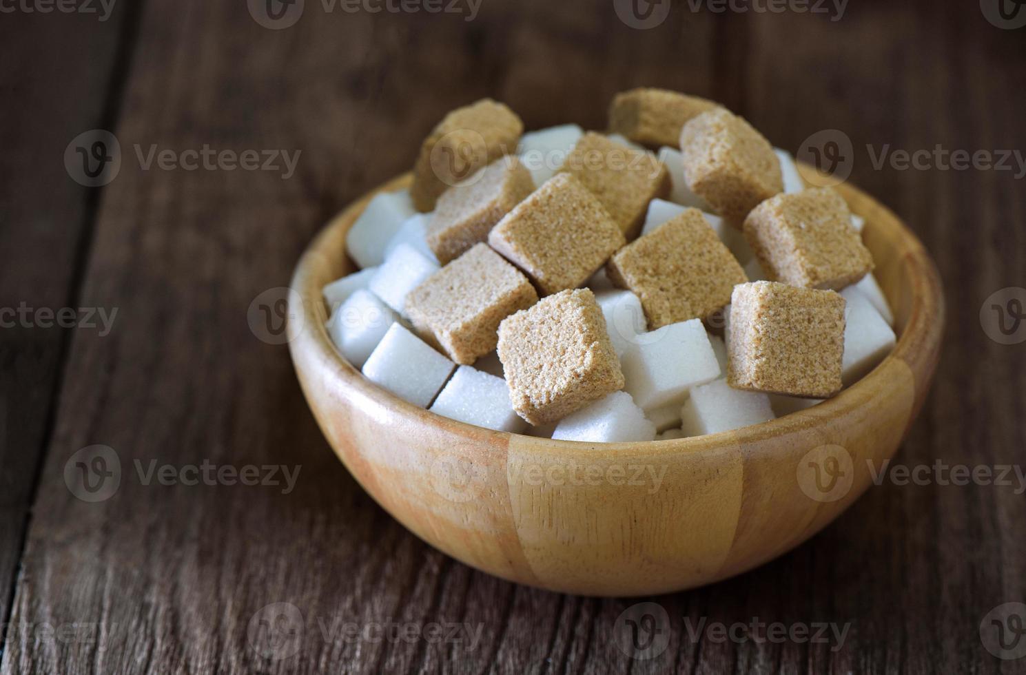 zollette di zucchero in ciotola di legno su tavola di legno foto