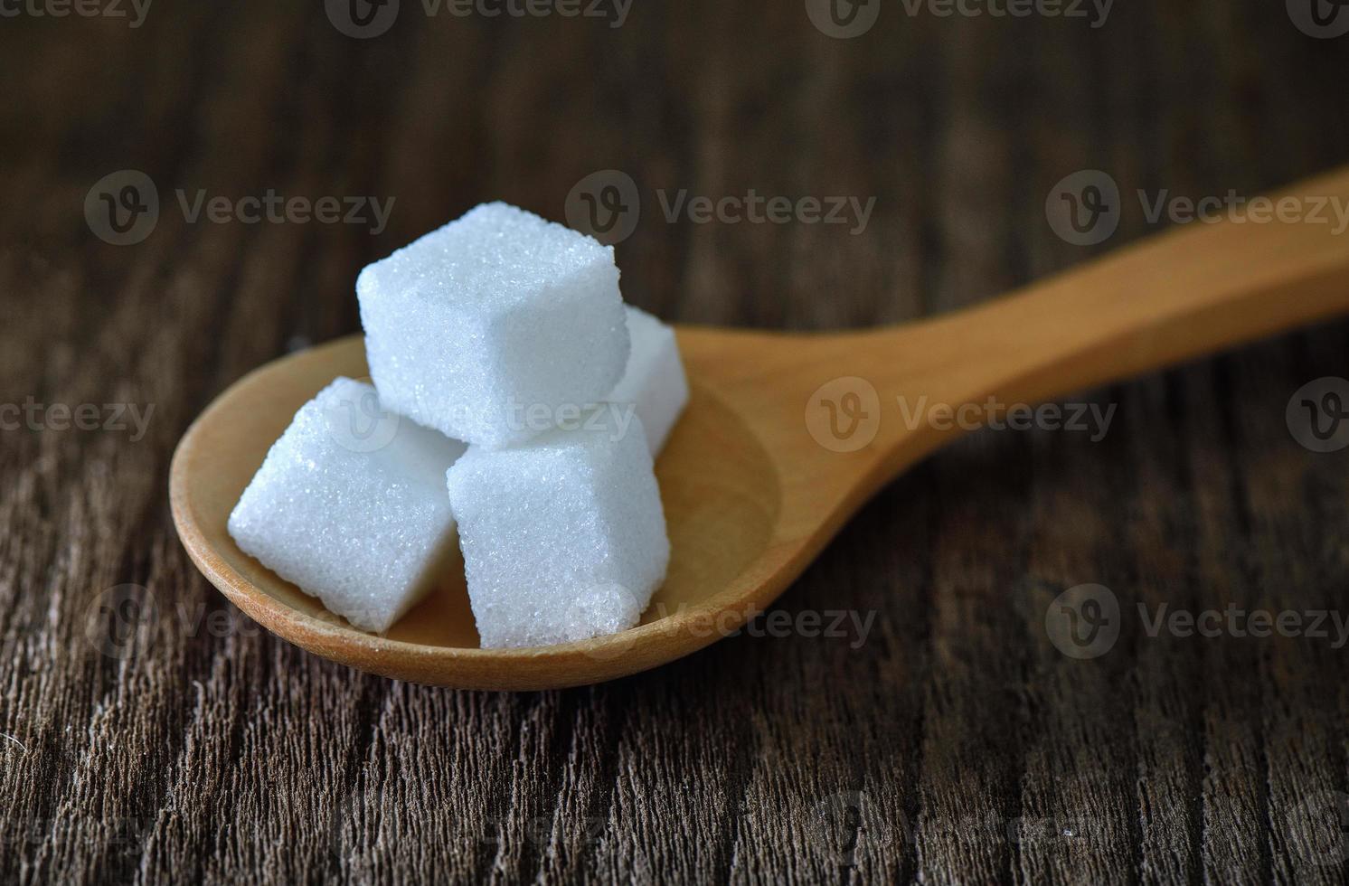 zollette di zucchero in cucchiaio di legno su tavola di legno foto