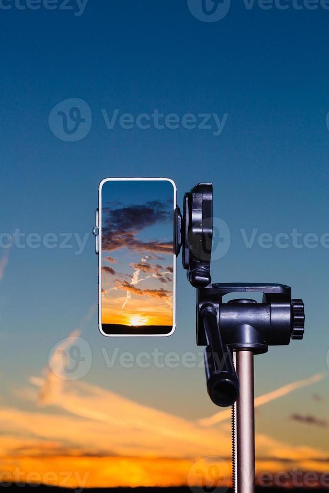 smartphone su treppiede che cattura l'immagine del tramonto in modalità verticale foto