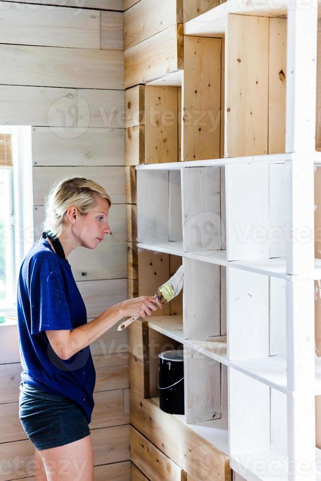 donna che applica il primo strato di vernice su una libreria in legno foto