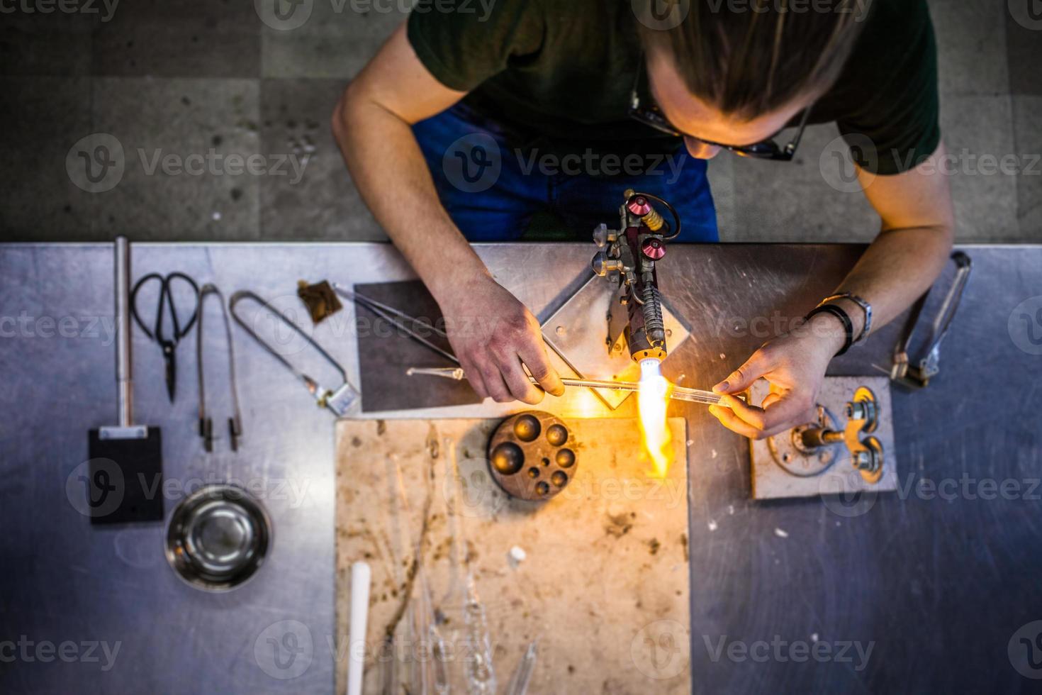 giovane soffiatore di vetro che lavora su una fiamma di una torcia con tubi di vetro foto