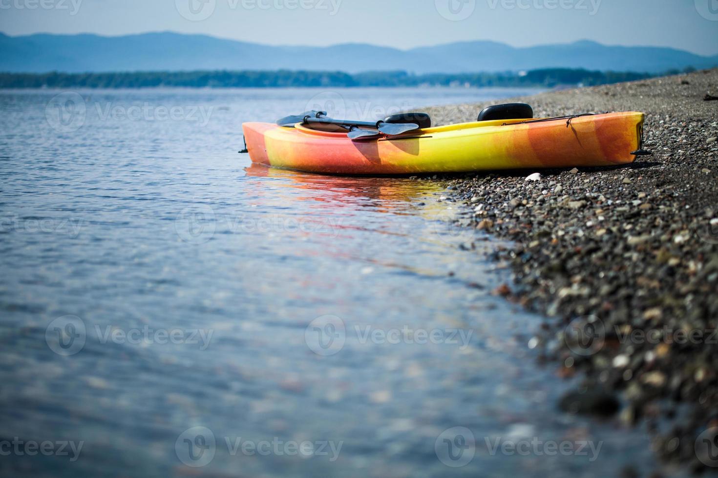 kayak arancione e giallo con remi in riva al mare foto