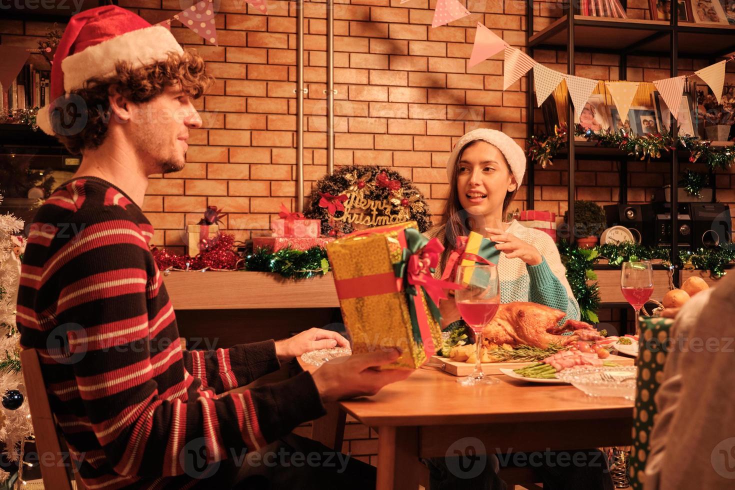 sorprendi tre amici e la famiglia dopo un pasto speciale facendo gioiosamente regali insieme e scambiandoli nella sala da pranzo di casa, decorata per la celebrazione del festival di Natale e la festa di capodanno. foto