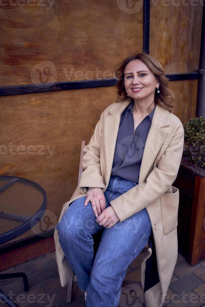 giovane adulto donna nel jeans e sabbia cappotto con grunge sfondo, arrugginito parete con caffè lettering foto