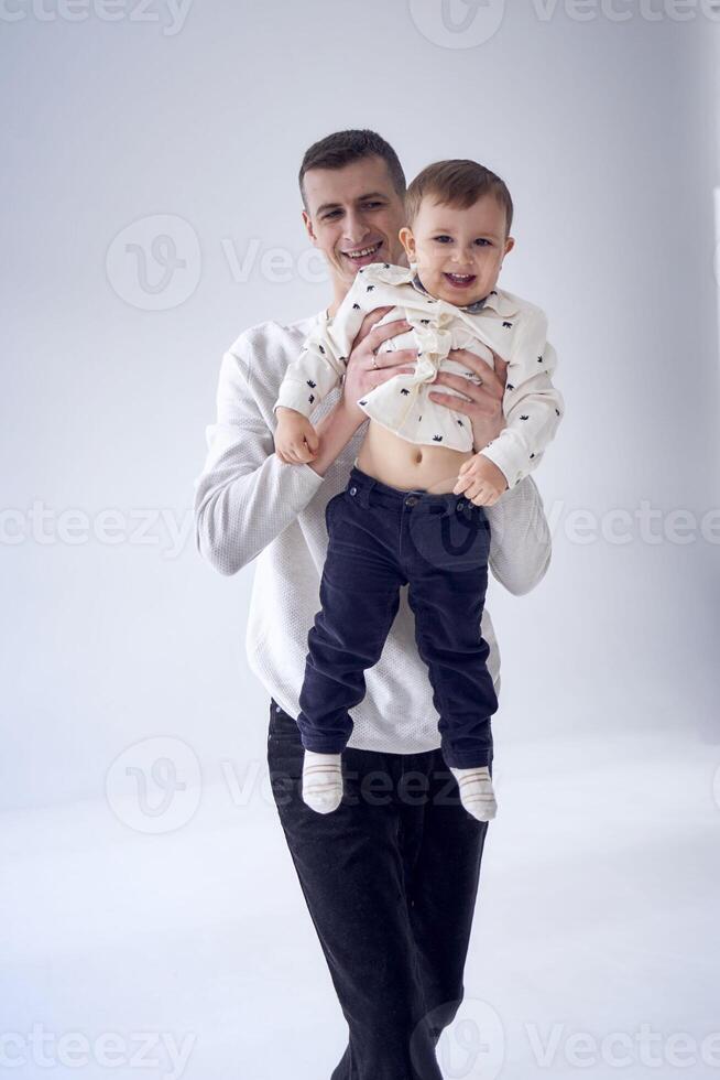 un' padre trasporta il suo figlio nel il suo braccia e giochi con lui nel un' minimalista studio foto