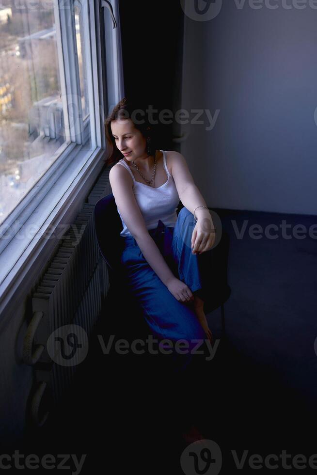 giovane adolescenziale ragazza combattente cervello cancro nel un' studio foto sparare seduta su un' sedia di il finestra