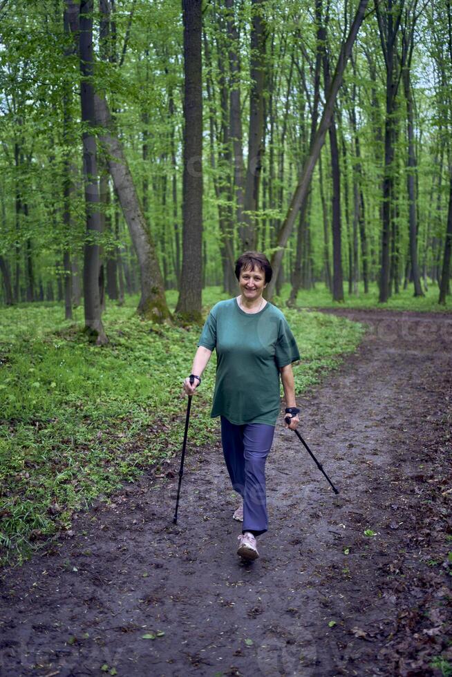 anziano donna è impegnato nel nordico a piedi con bastoni nel il primavera foresta foto
