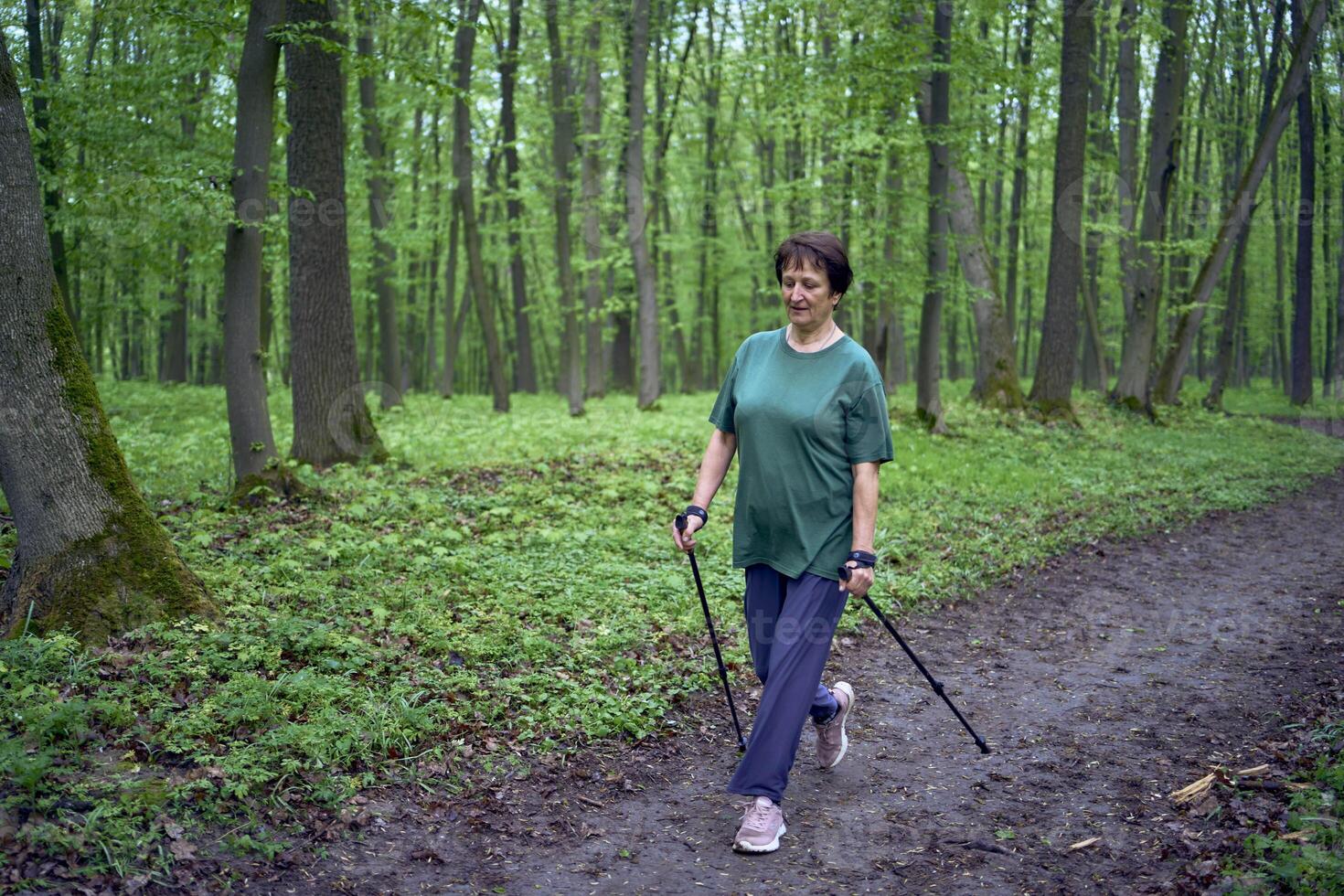 anziano donna è impegnato nel nordico a piedi con bastoni nel il primavera foresta foto