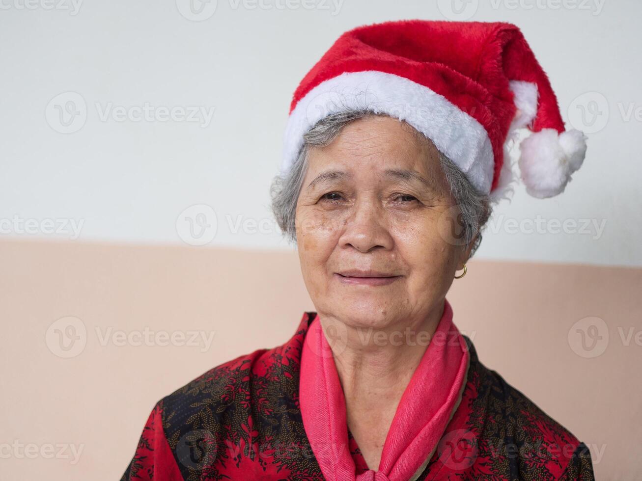 anziano donna indossare un' Santa Claus cappello e guardare a il telecamera. concetto di anziano persone e Natale e nuovo anno Festival foto