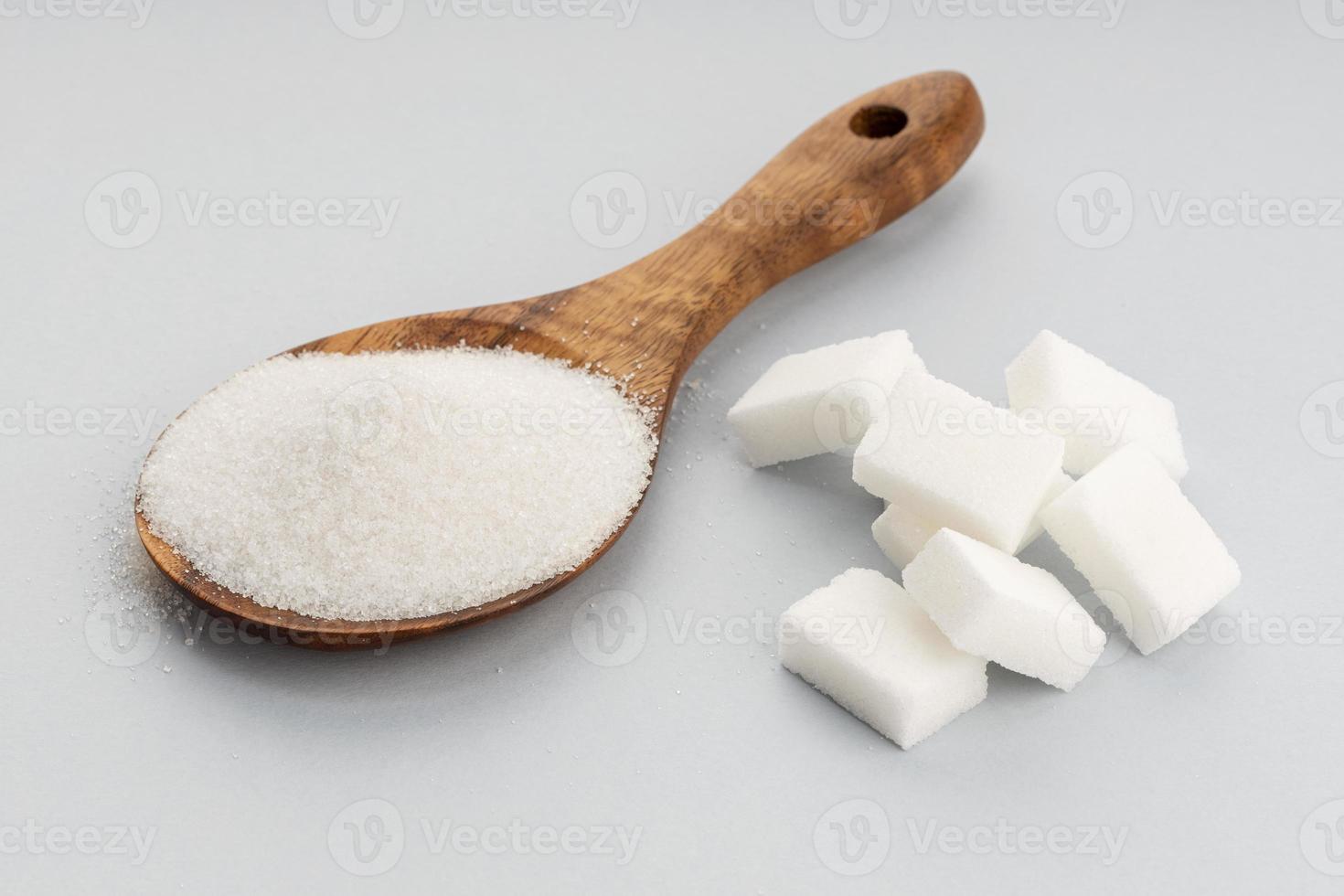 zucchero in cucchiaio di legno e cubetti di zucchero su sfondo grigio. avvicinamento foto