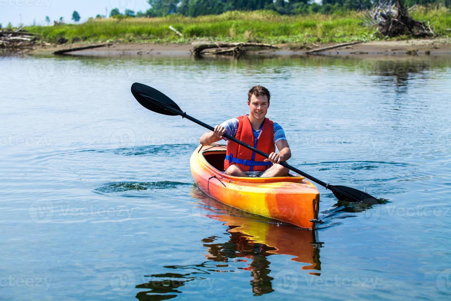 uomo con giubbotto di sicurezza in kayak da solo su un fiume calmo foto