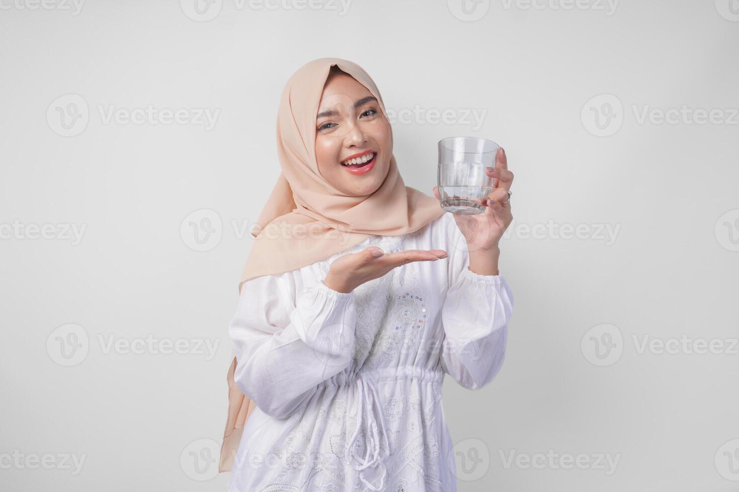 contento giovane asiatico musulmano donna nel un' velo hijab puntamento per un' bicchiere di chiaro acqua lei tiene. Ramadan annuncio pubblicitario concetto foto