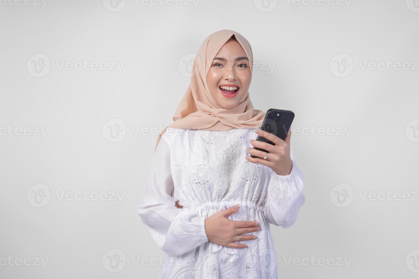 ritratto di giovane asiatico musulmano donna nel bianca vestito e hijab sensazione Affamato mentre guardare a sua Telefono per ordine delizioso cibo dopo digiuno, isolato su bianca sfondo foto